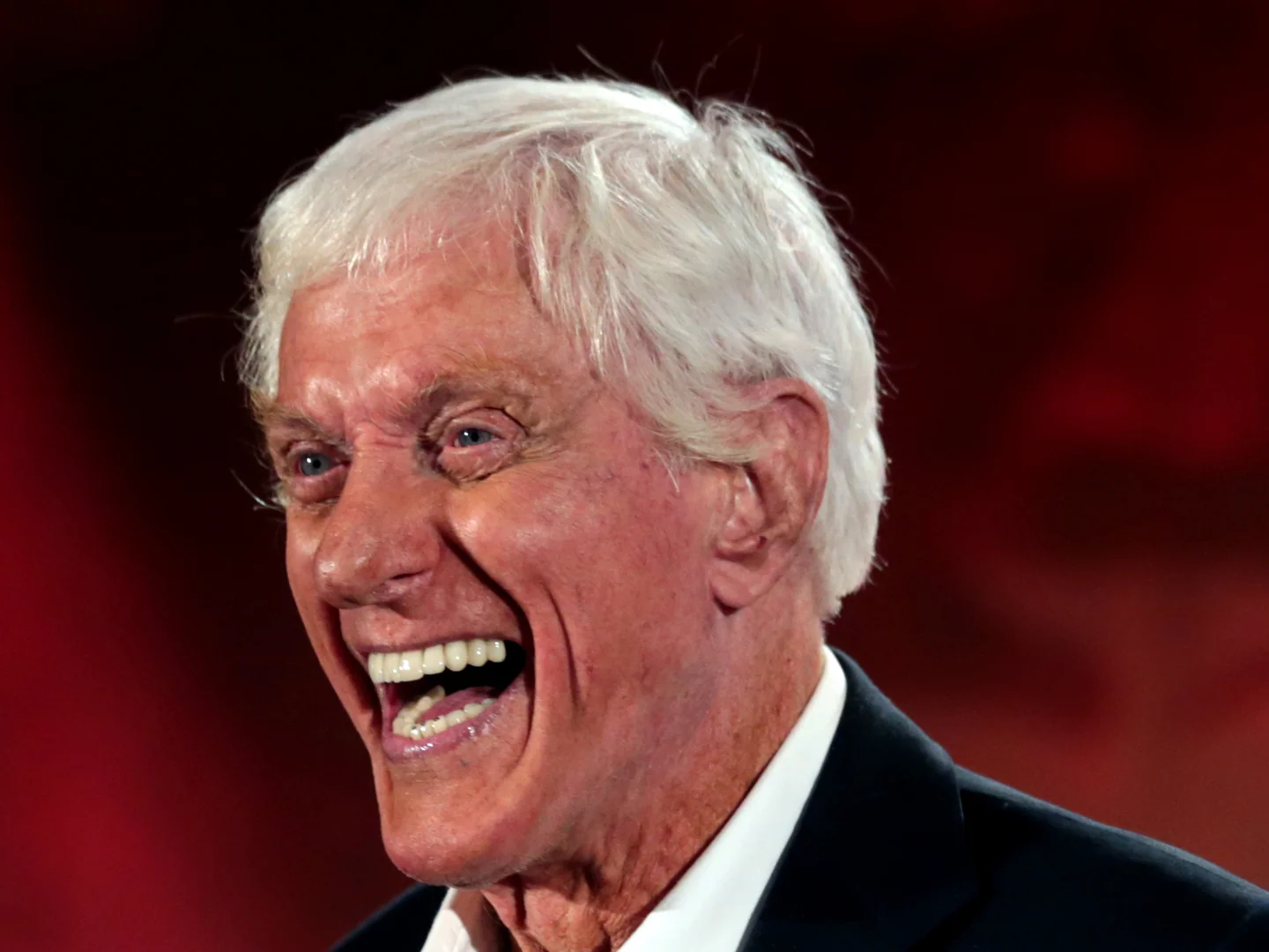 Dick Van Dyke, white-haired, in a dark jacket and white shirt, laughing
