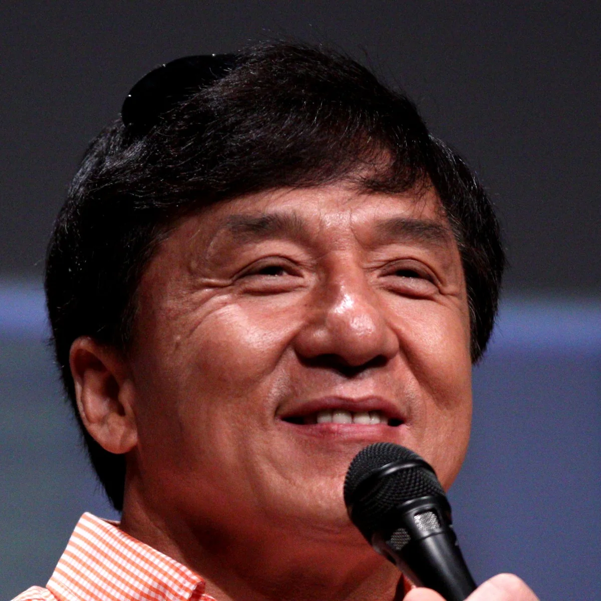 Jackie Chan, smiling, speaks into a microphone